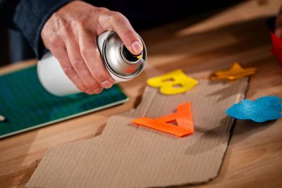 A hand applies spray adhesive to felt letters.