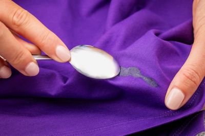 A person is scraping away dried glue from a purple shirt.