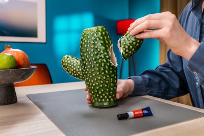 Hand brengt een deel van een kapotte keramiekcactus naar het andere deel van de keramieken cactus.