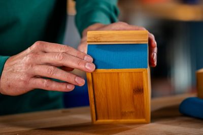 Uma mão mostrando a caixa de madeira customizada com uma faixa de tecido azul colada nela.