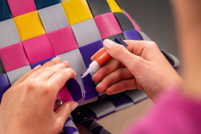 Uma mão aplicando Super Bonder Loctite no conserto de uma bolsa feminina colorida.