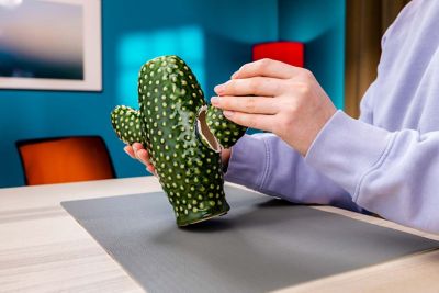 Una mano vuelve a pegar una pieza rota en un cactus de cerámica.