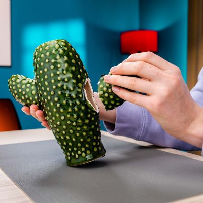 A close up of a person’s hands holding a broken green ceramic plant pot shaped like a cactus.