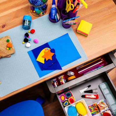 Various craft materials, scissors, glue, crayons, and paper are laid out on a wooden worktable.