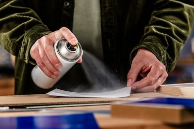 A person holds a can of spray adhesive in their hand and sprays it on the back of a photo.