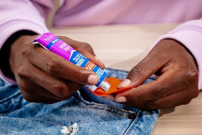 A hand applies glue to an orange patch of fabric over a pair of jeans with a hole.