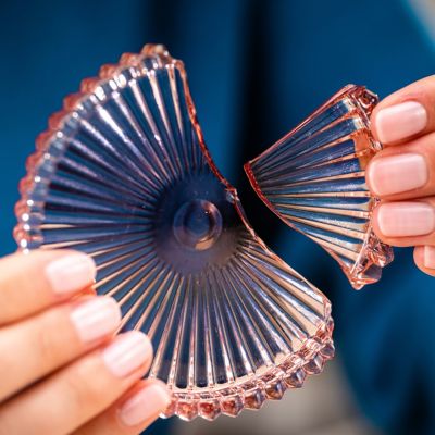 Two hands in close-up holding two parts of a broken pink glass coaster.