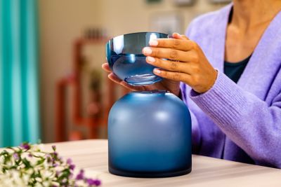 A hand holds the upper part of a broken blue vase over the bottom one. 