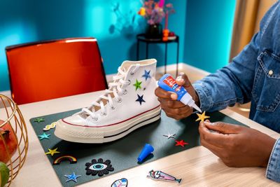 A person applies glue to a star-shaped patch. Next to it is a fabric sneaker with patches on it.