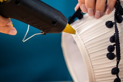 Glue is applied to the edge of a lampshade from a hot glue gun.