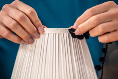 A person is gluing a border on a lampshade.