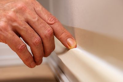 A hand runs a finger over a fresh baseboard sealant; the edges are taped. 
