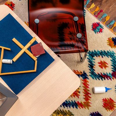 A table with crafting utensils on it, a table next to it, and a plastic bottle of glue on the carpet.