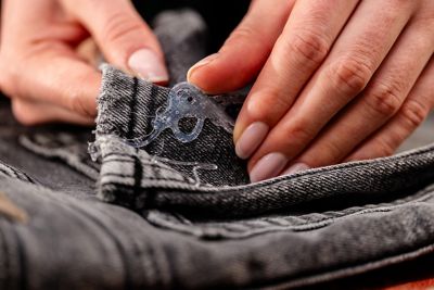 A hand removes a hardened piece of glue from a pair of jeans.