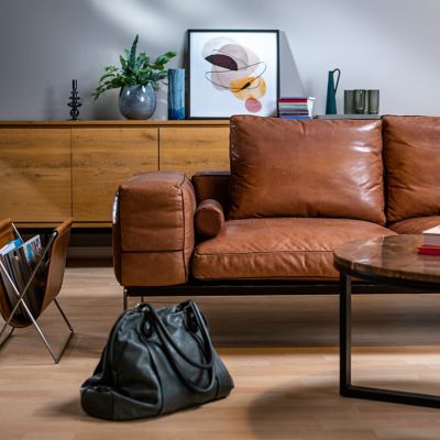 A leather couch in a living room with a leather bag in front of it.