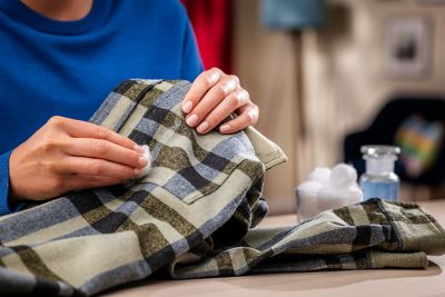 A hand rubs a cotton ball over a stain on a shirt.