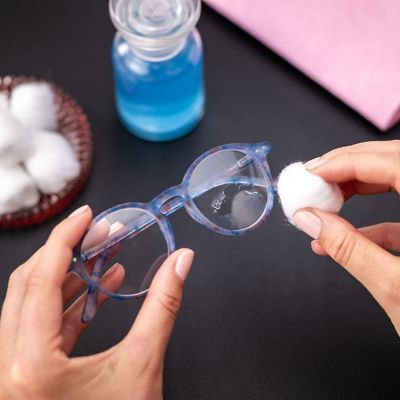 One hand holds a pair of glasses soiled with glue, the other a cotton ball.