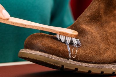 A person removes a glue stain from a leather shoe with a toothbrush.