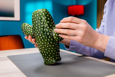 A hand presses a broken part of a cactus-shaped vase back on its place with glue.