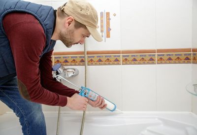 Caulk being applied to a white bathtub in a clean room