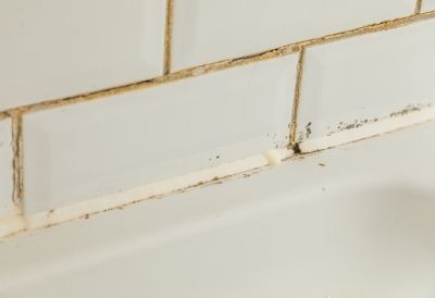 An off-white bathtub with cracked seals and faded tiles 