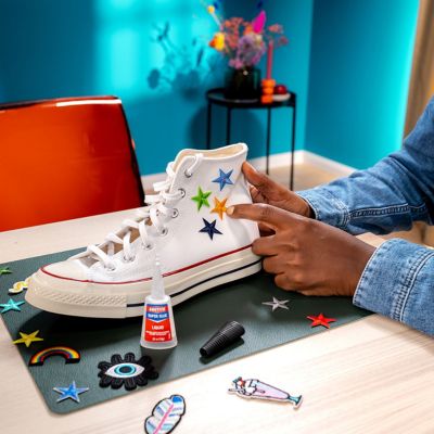 A person presses fabric stars onto a white fabric shoe, next to it is a bottle of Loctite Super Glue.