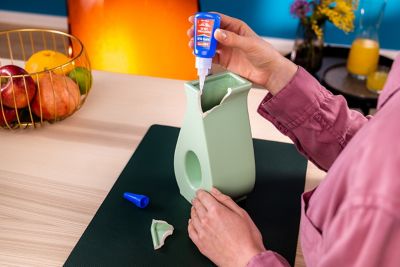 A person applies Loctite Super Glue Professional Liquid to the edges of a broken vase.
