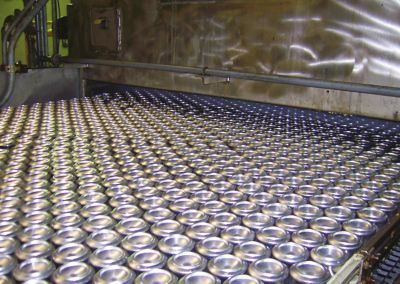 Hundreds of metal beverage cans in a conveyor belt entering washer