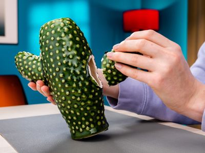 Eine Hand hält den abgebrochenen Arm eines Porzellan-Kaktusses vor die Bruchstelle.