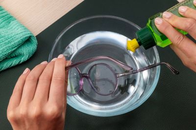 Eine Person entfernt Sekundenkleber mit Spülmittel und Wasser von einer Brille.
