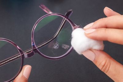Eine Person tupft mit etwas Baumwolle auf ein Brillenglas.