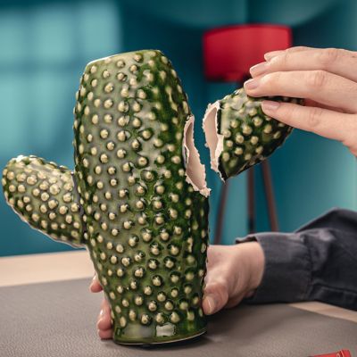 Hand brengt twee onderdelen van een kapotte decoratieve cactus van keramiek samen.