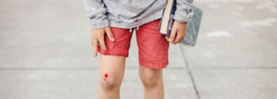 Un genunchi zgâriat, sângerând al unui băiat, focusul în fotografie este pe picioarele lui