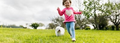 Küçük bir kız bir çayırda gülerek koşar, arka planda küçük beyaz bir köpek onu takip eder.