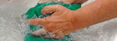 Hände waschen ein grünes Kleidungsstück in klarem Wasser
