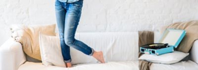Kot pantolonlu bir kadın hafif bir kanepede duruyor, sadece bacakları görünüyor.