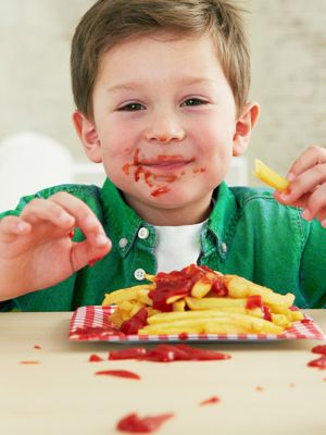 Junge mit Ketchup in Gesicht isst Pommes mit Ketchup