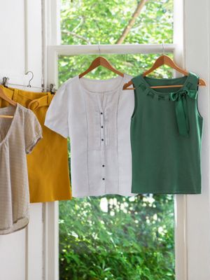 Bunte kleidungsstücke hängen auf kleiderbügeln vor einem fenster mit blick ins grüne