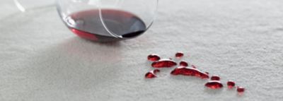 Ένα αναποδογυρισμένο ποτήρι με κόκκινο κρασί, δίπλα στο λευκό χαλί μερικές σταγόνες κρασί.