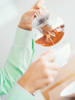 Frau gießt Tee aus Glaskanne in weiße Porzellantasse