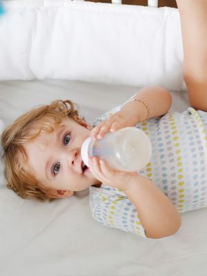 Baby liegt auf Bett mit Trinkflasche in der Hand