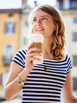 Blonde Frau in einem blau weiß gestreiften T-Shirt mit Kaffeefleck hält Kaffeebecher in der Hand