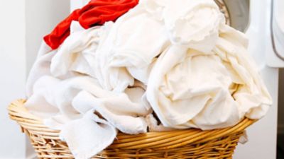 Geflochtener Korb voll mit weißer Wäsche und einem roten Kleidungsstück.