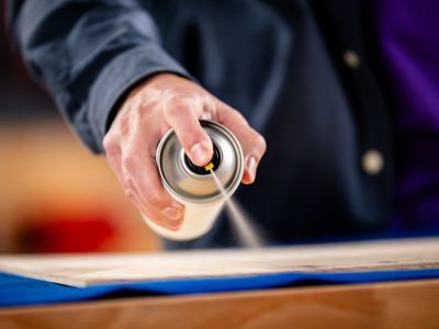 Una persona con una lata en sus manos aplica adhesivo a una superficie de madera.