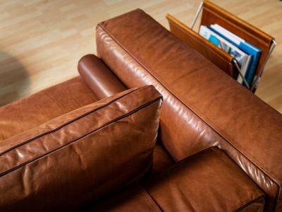 Un sofá de cuero color café que está al lado de un revistero.