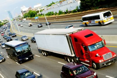 Semi-truck driving on a highway with a black bus and numerous cars