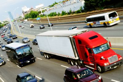 Semi-truck driving on a highway with a black bus and numerous cars