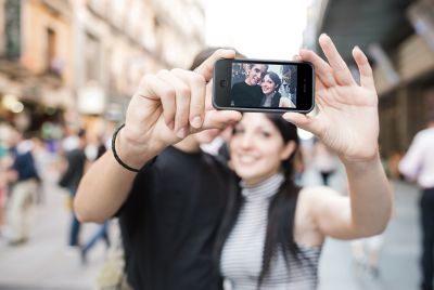 Photo of young couple holding a smartphone and taking a selfie background is blurred busy city sidewalk with picture perfect clarity of the young couple on the display screen of their smarphone device shutterstock ID 159175196