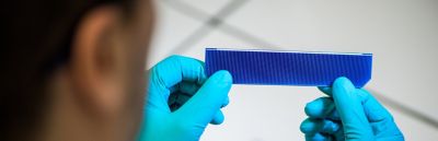 Photo of lab technician wearing blue gloves inspecting blue solar cell to be assembled into solar panel using a shingling approach and electrically conductive silver adhesive epoxy