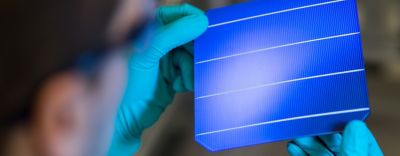 Photo of lab technician wearing blue gloves inspecting blue solar cells assembled into solar panel using a shingling approach and electrically conductive silver adhesive epoxy